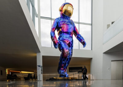 A large reflective metallic astronaut sculpture with handwritten text displayed in a modern white building atrium.