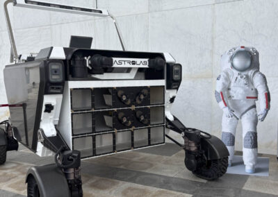 An AstroLab planetary rover vehicle displayed next to an astronaut in a white spacesuit against a marble wall.