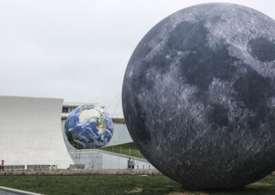 Giant detailed inflatable models of planet Earth and the Moon installed on outdoor museum grounds.