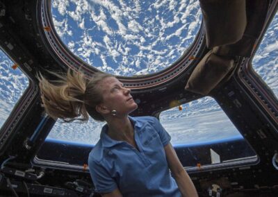 Astronaut Dr. Karen Nyberg with her hair floating in zero gravity, looking out the circular window of the International Space Station Cupola module at Earth below.