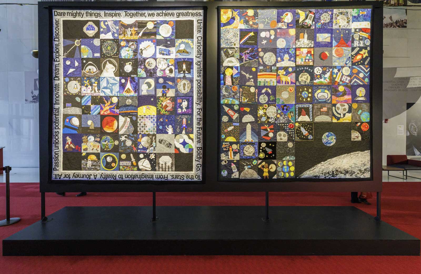 Two large museum exhibition panels displaying collaborative space-themed quilts composed of individual quilt blocks created by global community participants.