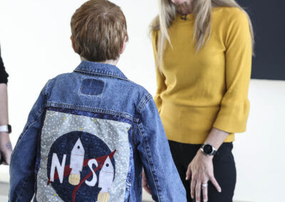 Astronaut Dr. Karen Nyberg smiling at a child wearing a denim jacket featuring a hand-stitched NASA rocket quilt patch during the Lunar Quilts event.