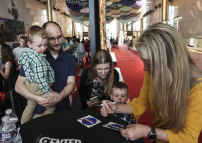 Astronaut Dr. Karen Nyberg signing NASA logo stickers for young festival visitors during "The Next Giant Leap: Lunar Quilts" exhibition.