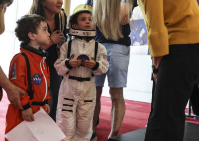 Astronaut Dr. Karen Nyberg leaning down to speak with two young boys wearing orange and white NASA suit costumes at the Lunar Quilts exhibition.